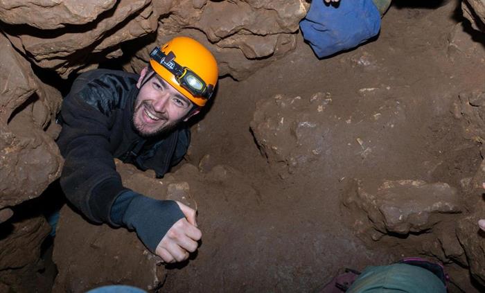 Smiling man wearing helmet climbing up through hole in cave